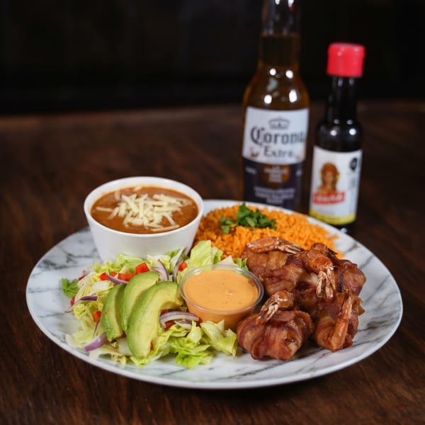 Bacon-wrapped shrimp, rice, beans, and salad with avocado, served with a Corona beer.
