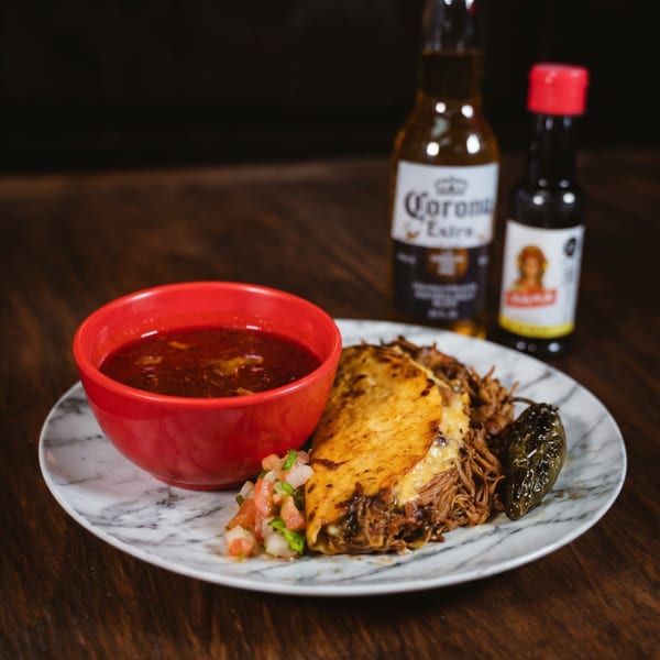 Birria tacos with consommé, pico de gallo, a grilled jalapeño, and a Corona beer.