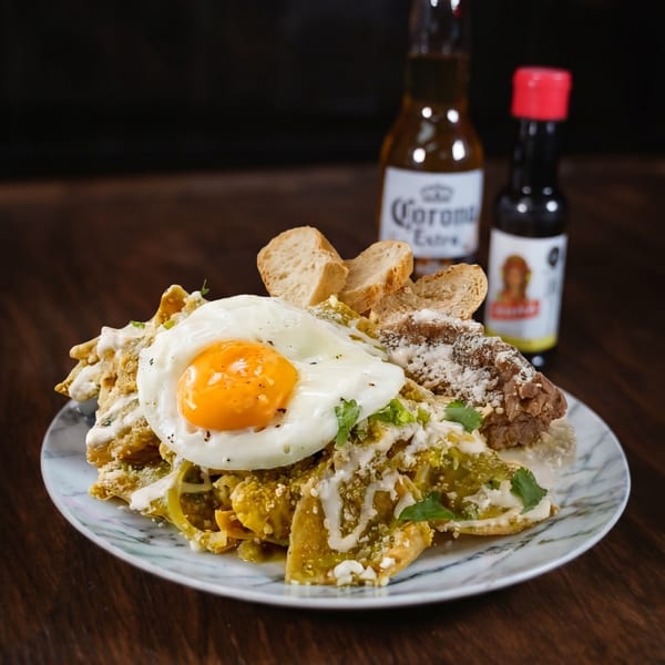 Chilaquiles with a fried egg, refried beans, and bread, served with a Corona beer and hot sauce.