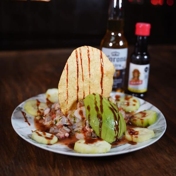 Ceviche with avocado, cucumber, and a tostada, served with a Corona beer and hot sauce.