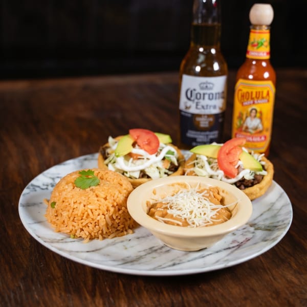 Plate with two sopes, Mexican rice, refried beans, a Corona beer, and Cholula hot sauce.